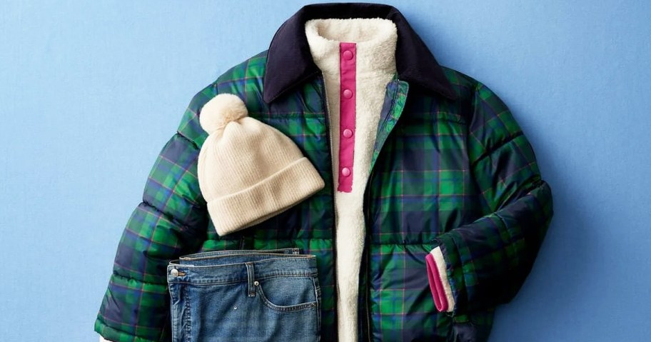 plaid puffer jacket laid out with white fleece, jeans, and white beanie