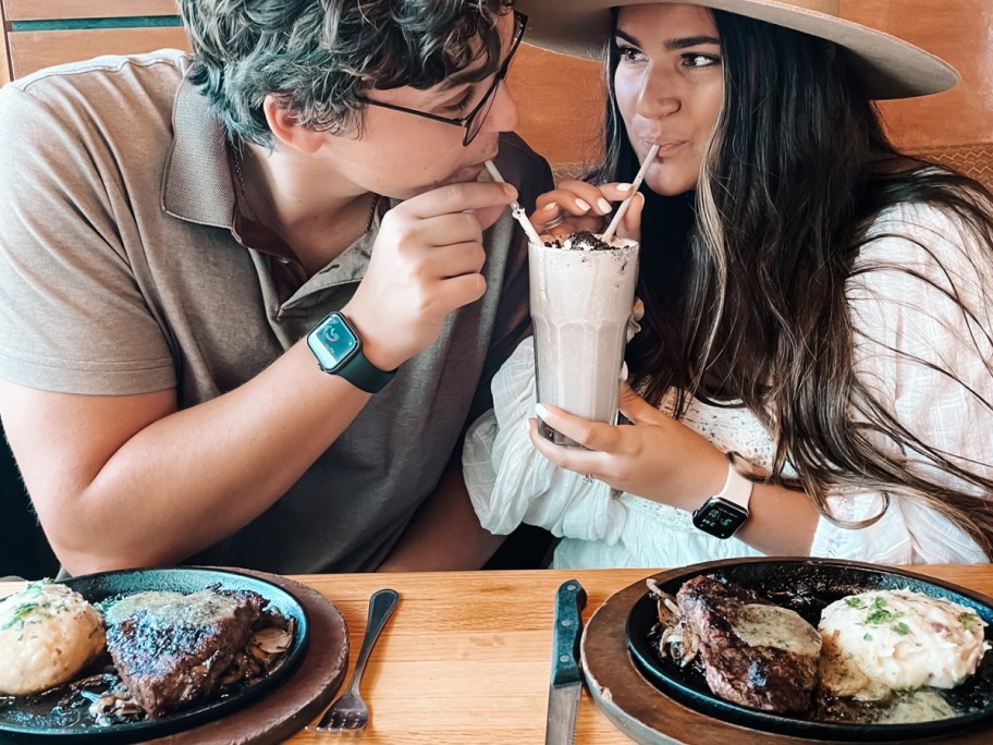 man and woman sipping a milkshake in front of plates of food