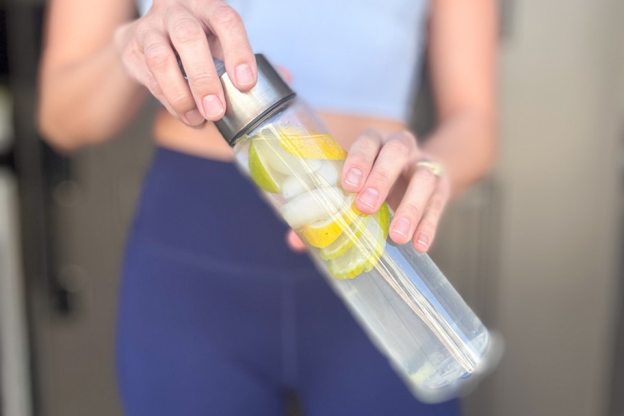 hands holding water bottle with lemons and limes