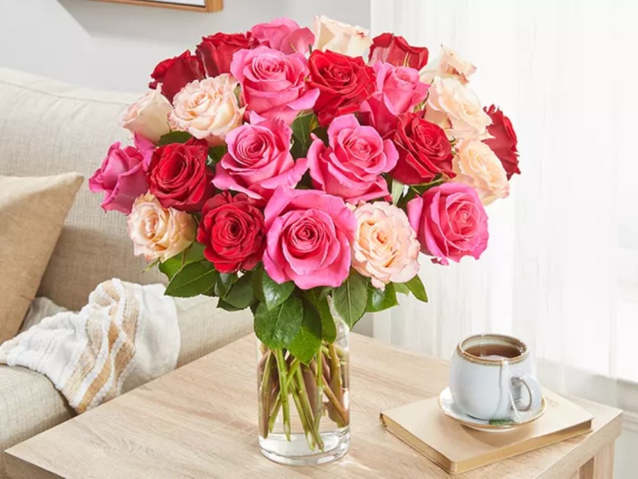 a vase filled with pink, red, and light peach color roses sitting on a side table