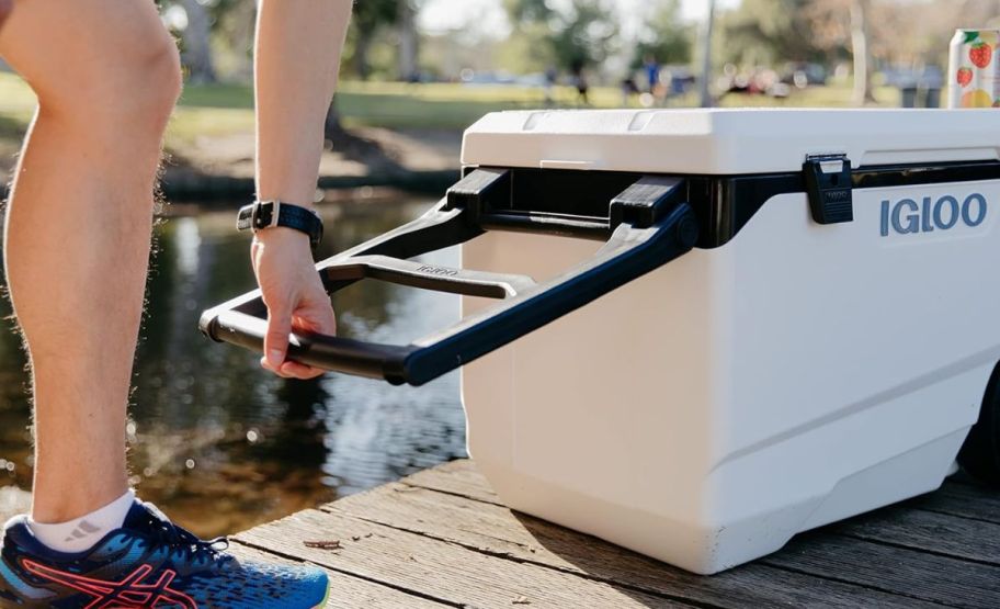 a mans hand grabbing the handle of a 90 qt igloo rolling cooler 