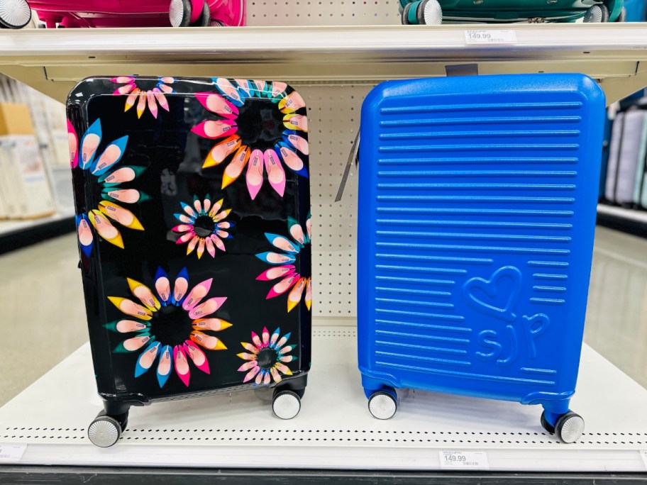 2 hardside spinner carryon size suitcases next to each other on a store display endcap - one is black with multicolor flowers and one is a solid bright blue color