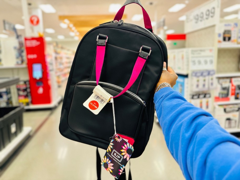 hand holding a black travel backpack with pink accents, Target store aisles in the background