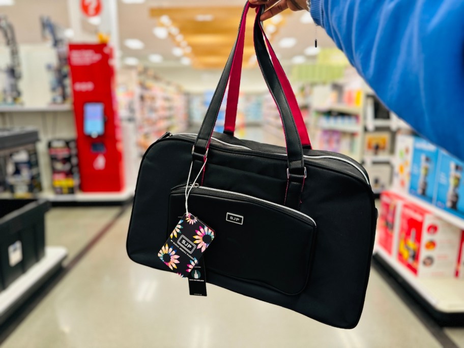 hand holding a black travel weekender bag with pink accents, Target store aisles in the background