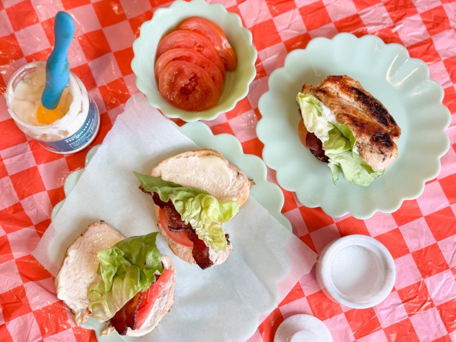 chicken breast BLT on green plates on pink and red checkered tablecloh