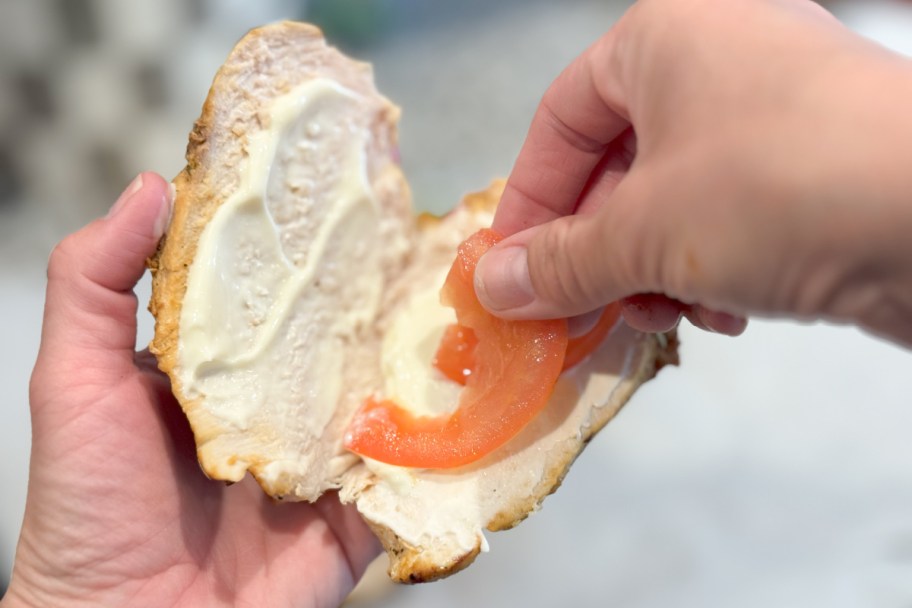 hand putting tomato on chicken breast sandwich