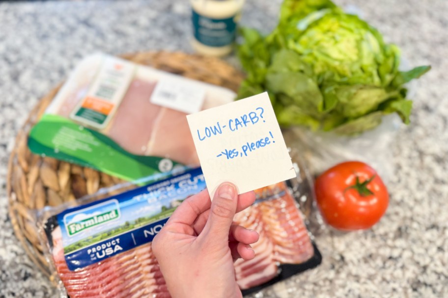 hand holding sticky note over bacon, chicken, lattuce, and tomato