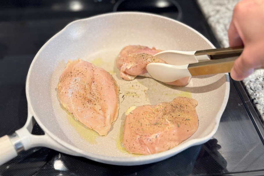 tongs grabbing chicken cooking in pan