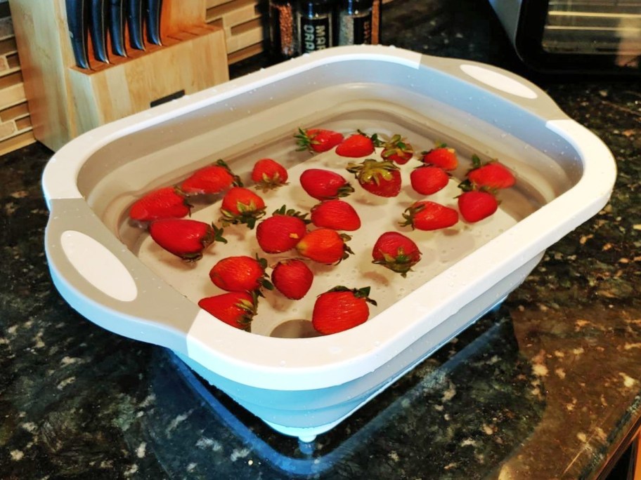 strawberries floating in water inside a collapsible colander cutting board