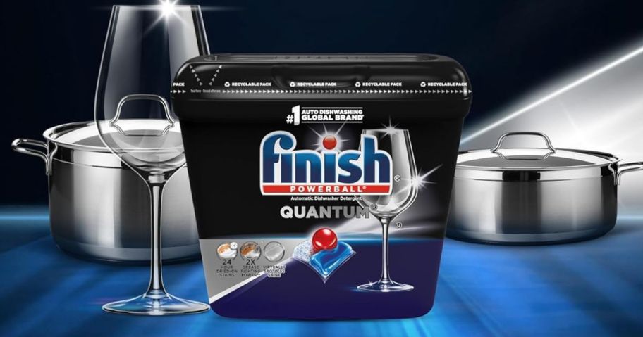 A tub of finish dishwasher pods next to clean dishes and glasses