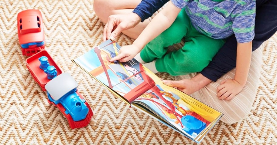 child sitting in parent's lap reading book near train toy