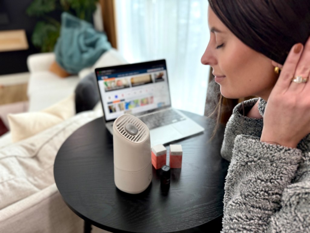 Woman breathing in humidified air from white portable humidifier on desk next to onlineputer