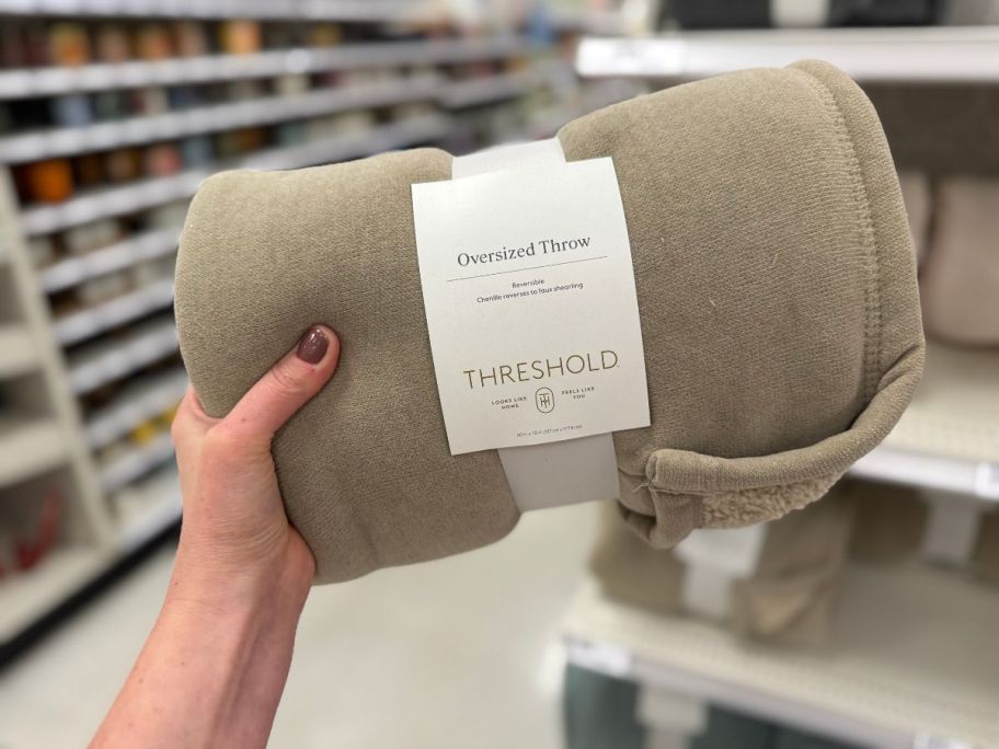 A person holding a tan blanket in a store