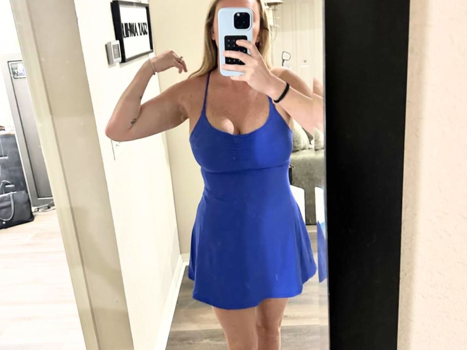 A woman is taking a picture of herself in the mirror wearing a blue athletic dress 
