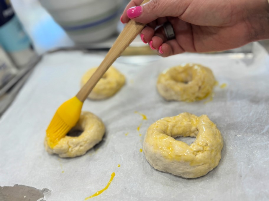 adding egg wash to the top of homemade bagels 