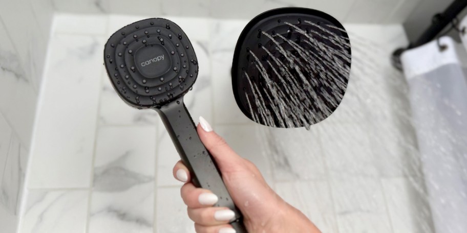 hand holding black showerhead with water onlineing out of fixed showerhead