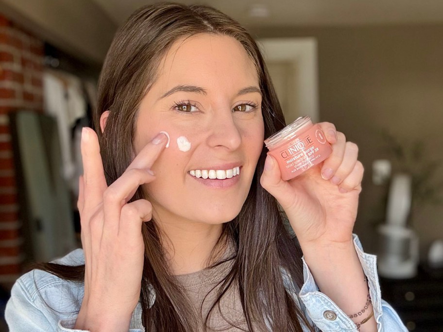 woman holding clinique moisture jar while putting cream on face 