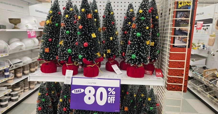 small Christmas trees on a store shelf with a sign that says 80% off