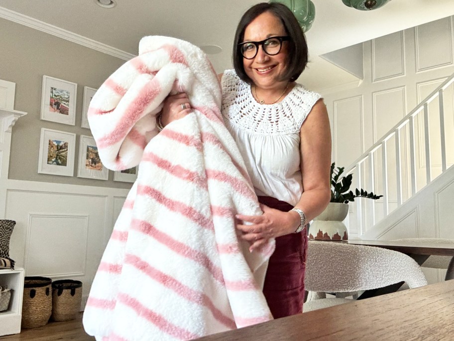 woman holding up a white and pink striped throw blanket