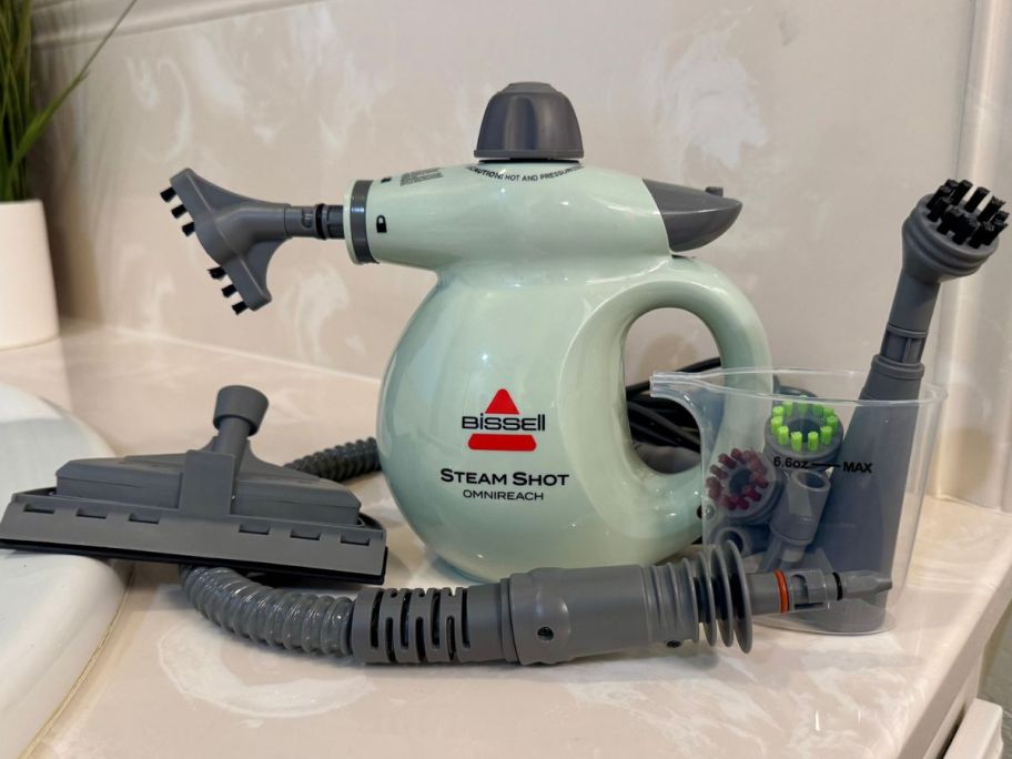 A Bissell Steam Shot Omnireach with accessories on the edge of a bathtub