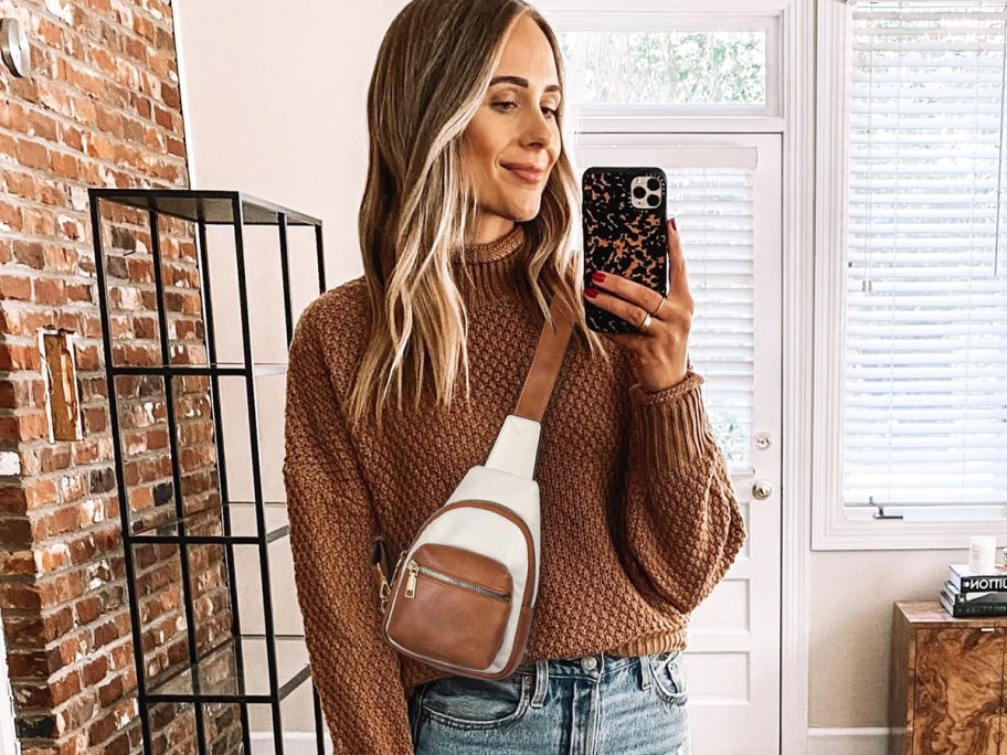 woman taking photo in mirror of her wearing a white/brown sling bag with a brown sweater