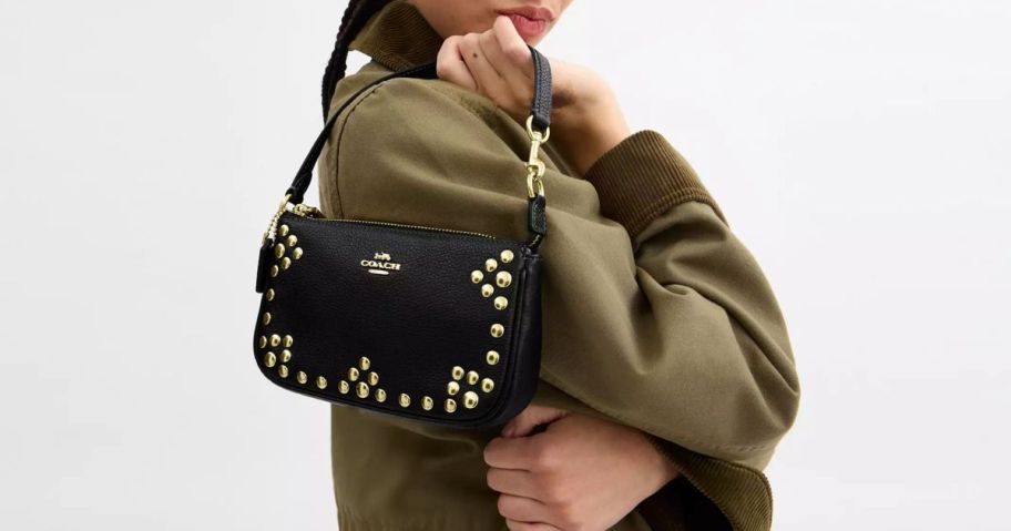 Woman holding a coach bag with rivets over her shoulder