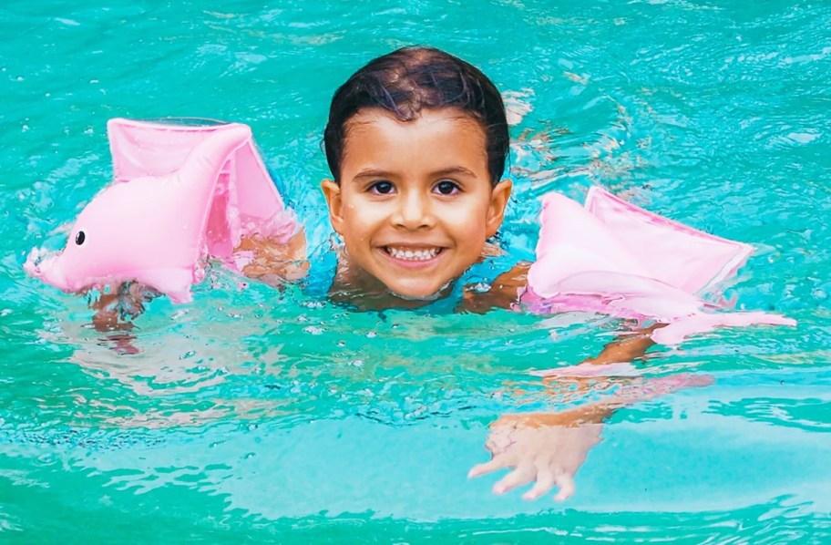 cild in pool with pink dolphin inflatable arm bands
