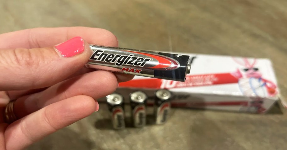 hand holding an energizer battery, more batteries on a table behind it
