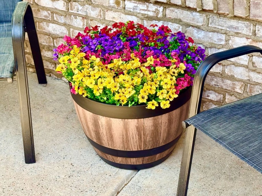 a wine barrel planter with colorful flowers in it in between 2 patio chairs