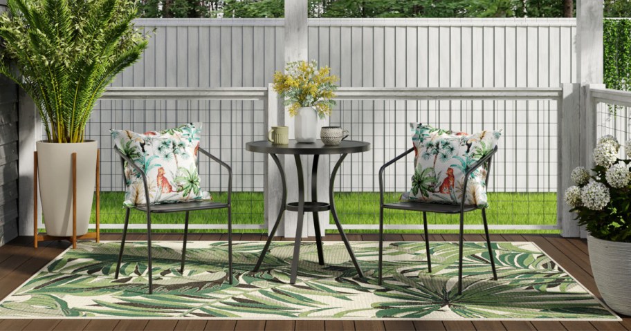 Black steel bistro set outside on deck on top of outdoor rug