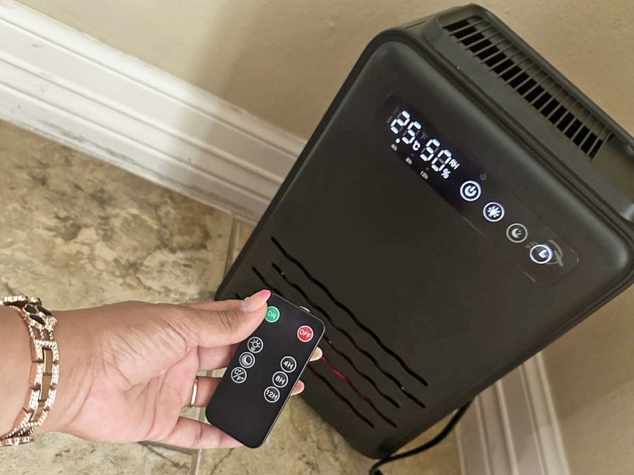 hand holding remote to black dehumidifier 