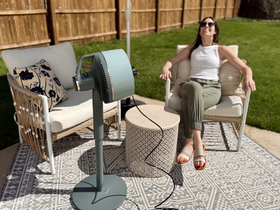 woman sitting on patio chair with blue Shark FlexBreeze Cordless Fan