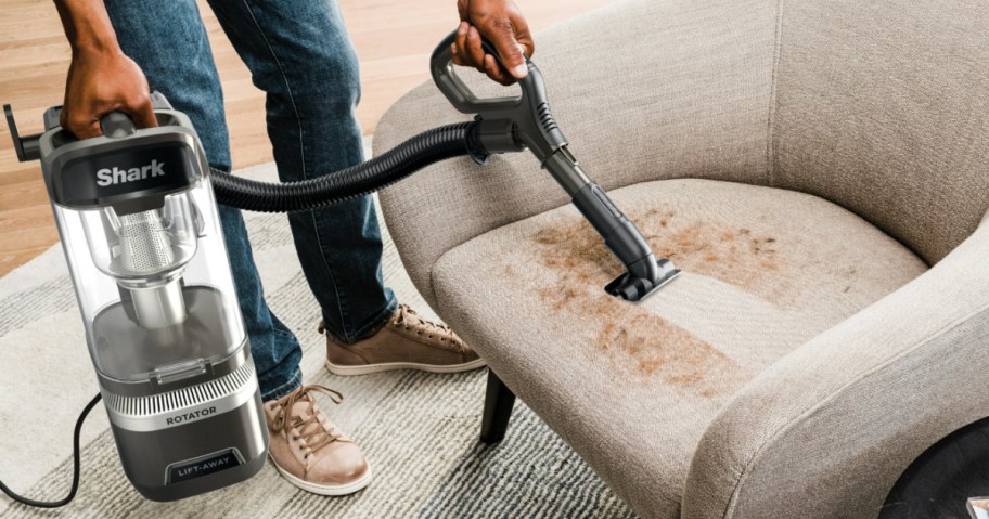 Person using handheld portion of shark rotator vacuum to clean upholstered chair