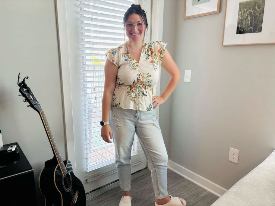 Woman posing in corner of room with light colored jeans and flutter sleeve top