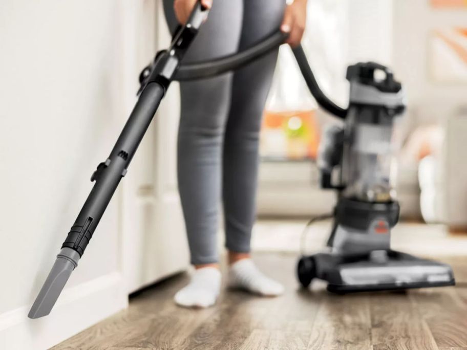 person using BISSELL Clean View Rewind Pet Upright Vacuum attachment along the wall