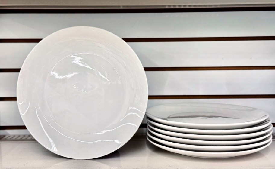 white ceramic plates stacked and standing up next to the stack on a store shelf