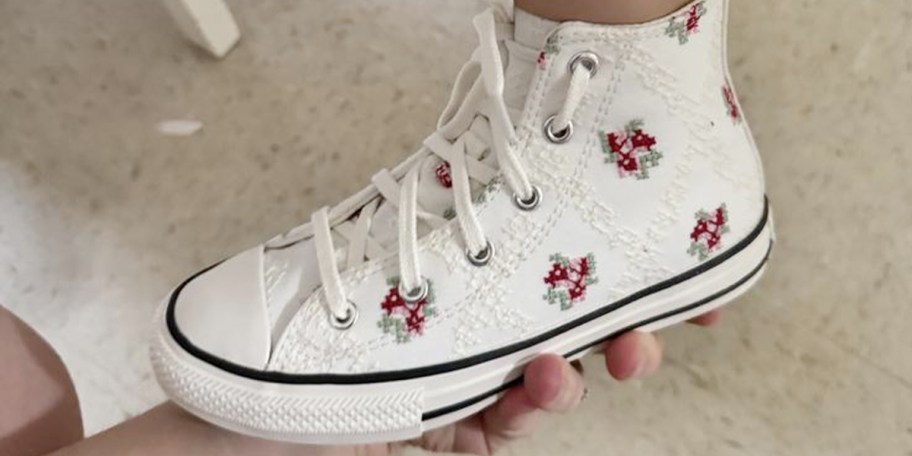 hand holding kids foot wearing white rose converse shoe