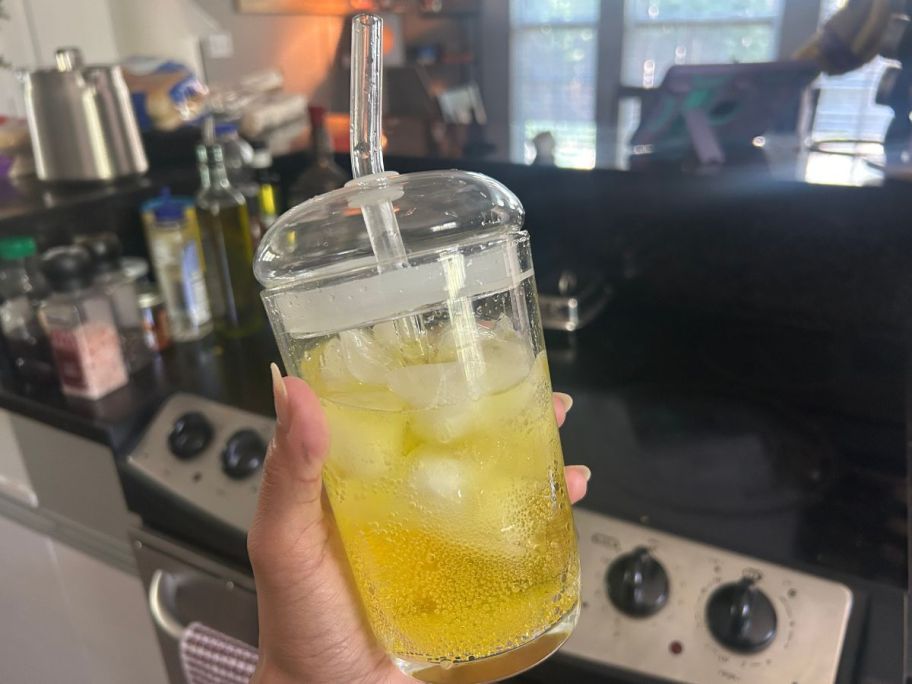 clear Better Homes & Gardens Dome Lid Glass Tumbler with yellow liquid in it in hand in kitchen