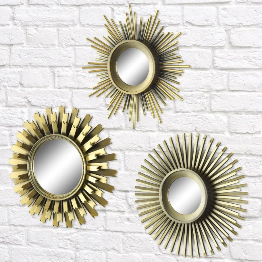 3 gold sun burst mirrors hanging on a white brick wall