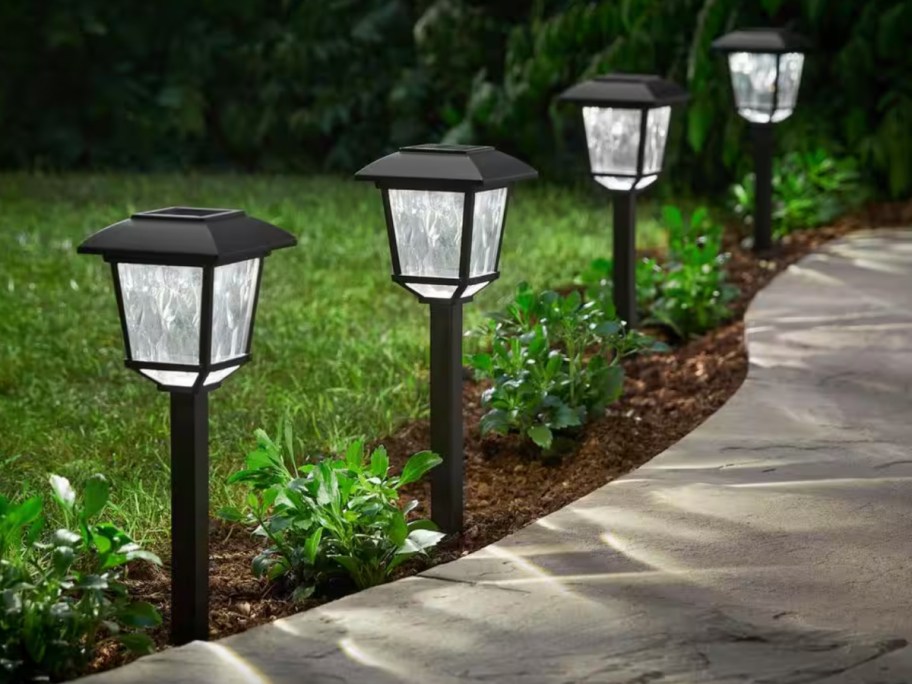 four black solar lights on a path