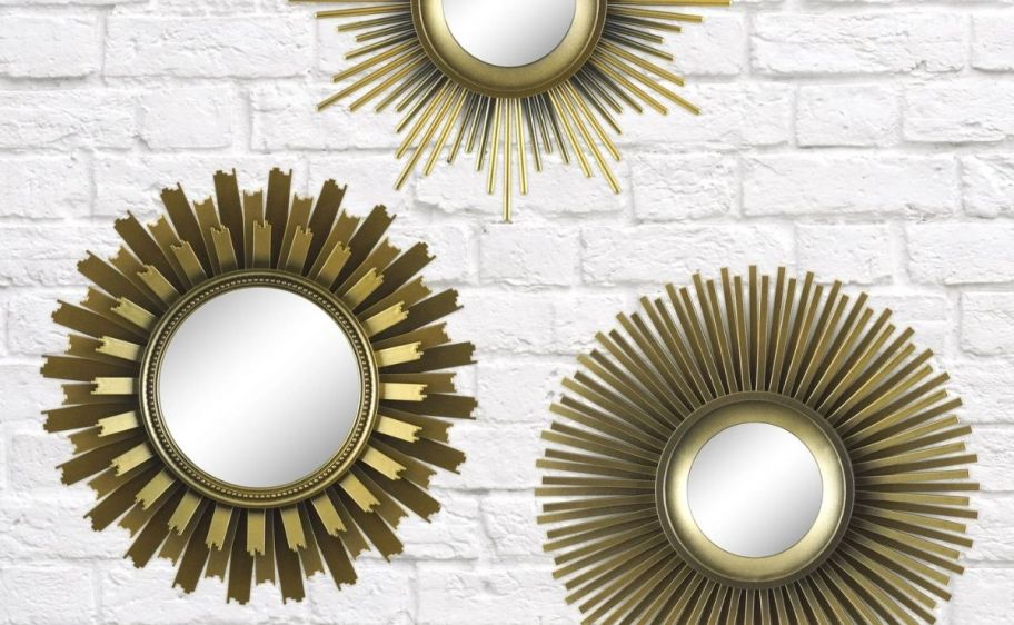 3 gold sun burst mirrors hanging on a white brick wall