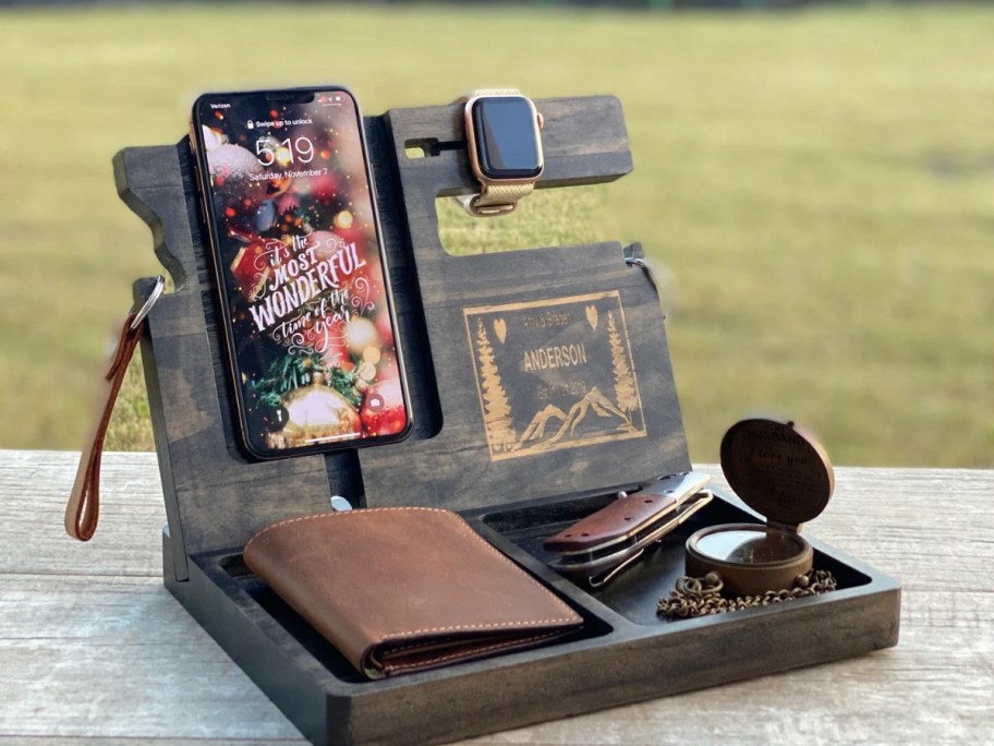 a wood docking station with a phone, watch, wallet, sunglasses on it