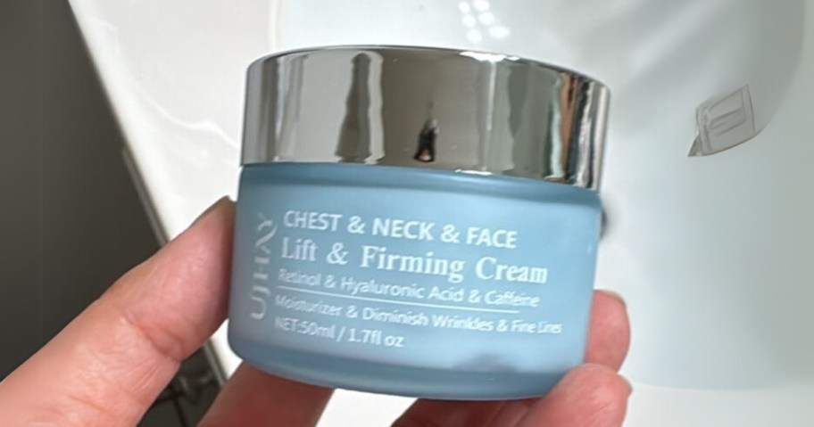 hand holding a jar of UJhay Firming Neck, Chest, & Face  Cream