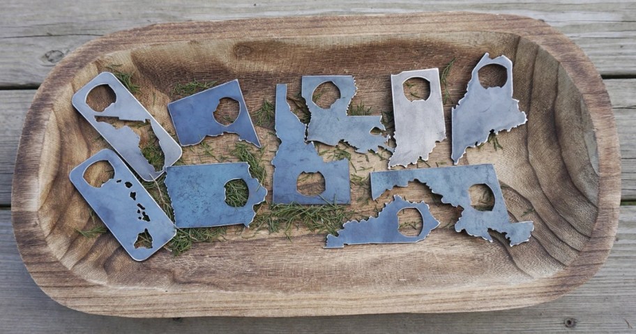 a wood bowl with steel US State shaped bottle openers