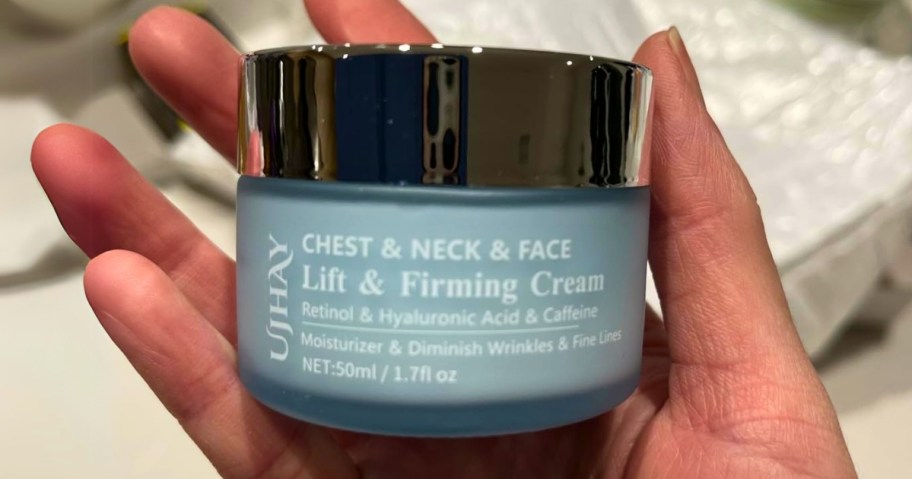 hand holding a jar of UJhay Firming Neck, Chest, & Face  Cream