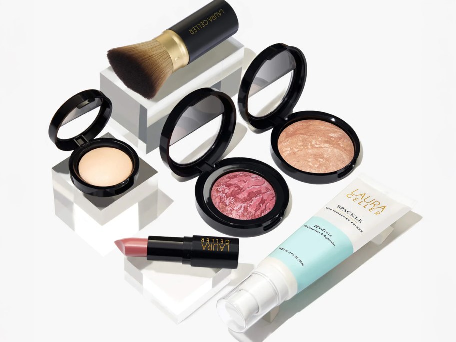 Laura Geller Cult Classics Full Face Kit featuring blush, bronzer, highlighter, lipstick, primer, and makeup brush on display blocks.