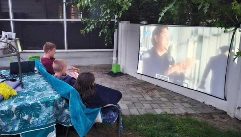 kids sitting outside watching projector movie on fence