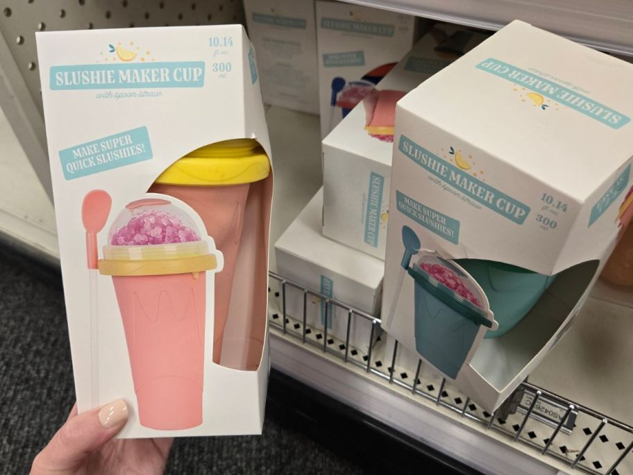 a pink and yellow Slushee Maker Cup box in hand next to a green one on a shelf in store