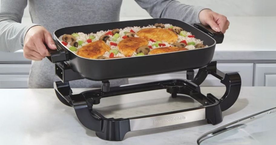 person holding Hamilton Beach 20.5" Durathon Ceramic Reversible Nonstick Electric Skillet and lifting it off of the heating element