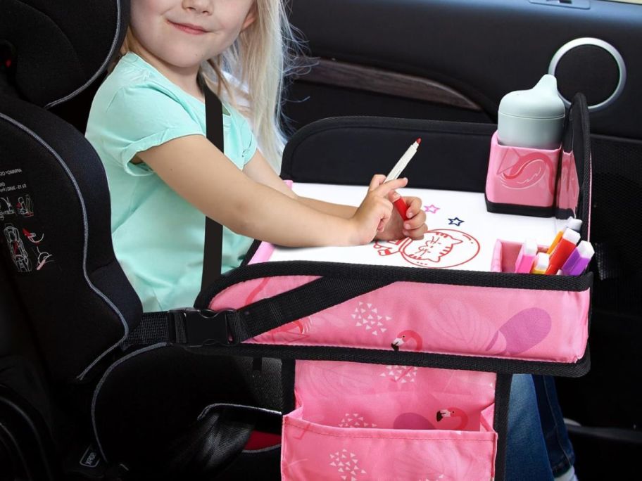 girl drawing on dry erase board on kids travel tray in car